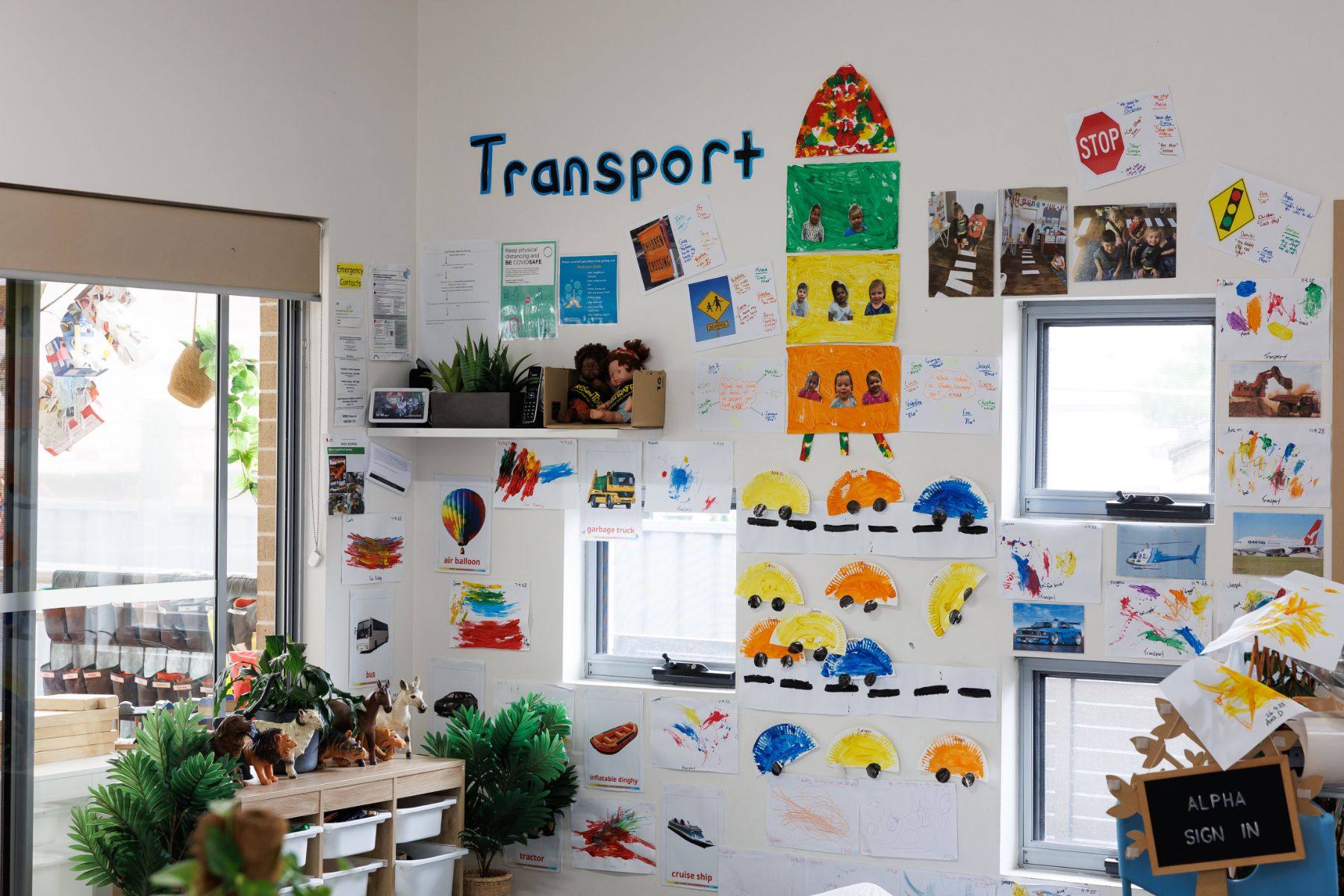 Transport-themed wall of children's artwork in the Omegas room